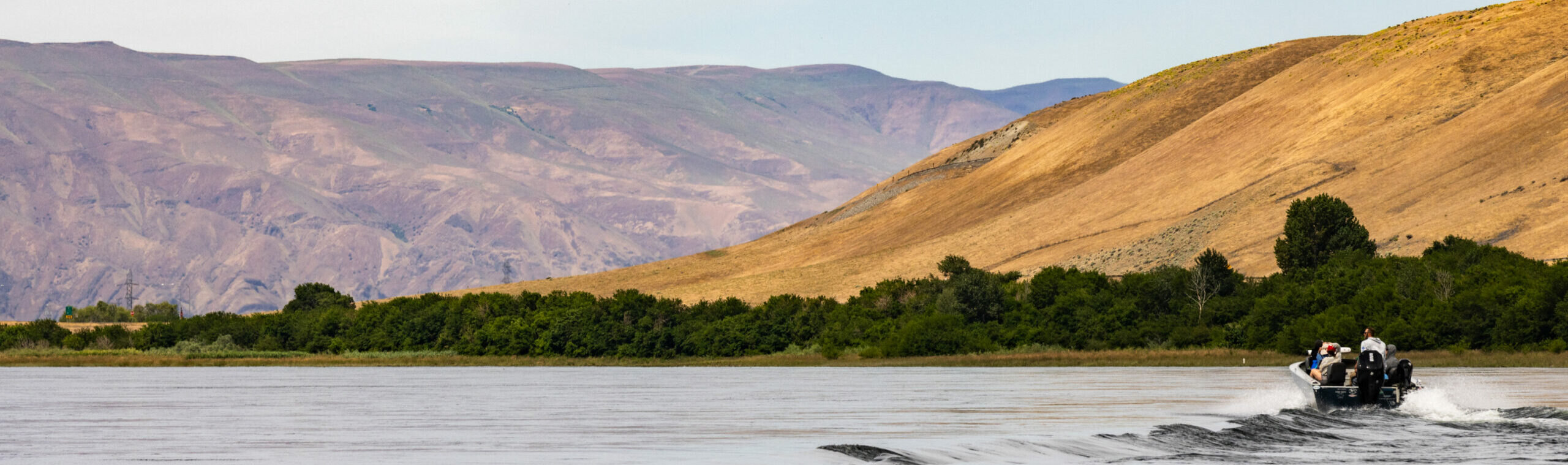 Boat on the river at Hanford Reach, with reactor in the background. Photo by Kelly Turso.